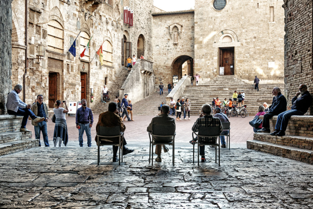 ältere Männer sitzend von hingen fotografiert, in einem offenen Raum mit Blick auf die Kirche in San Gimignano, Portfolio, Toskana Fotografie Workshop Panorama Landschaft 2018 photography Workshop in Tuscany