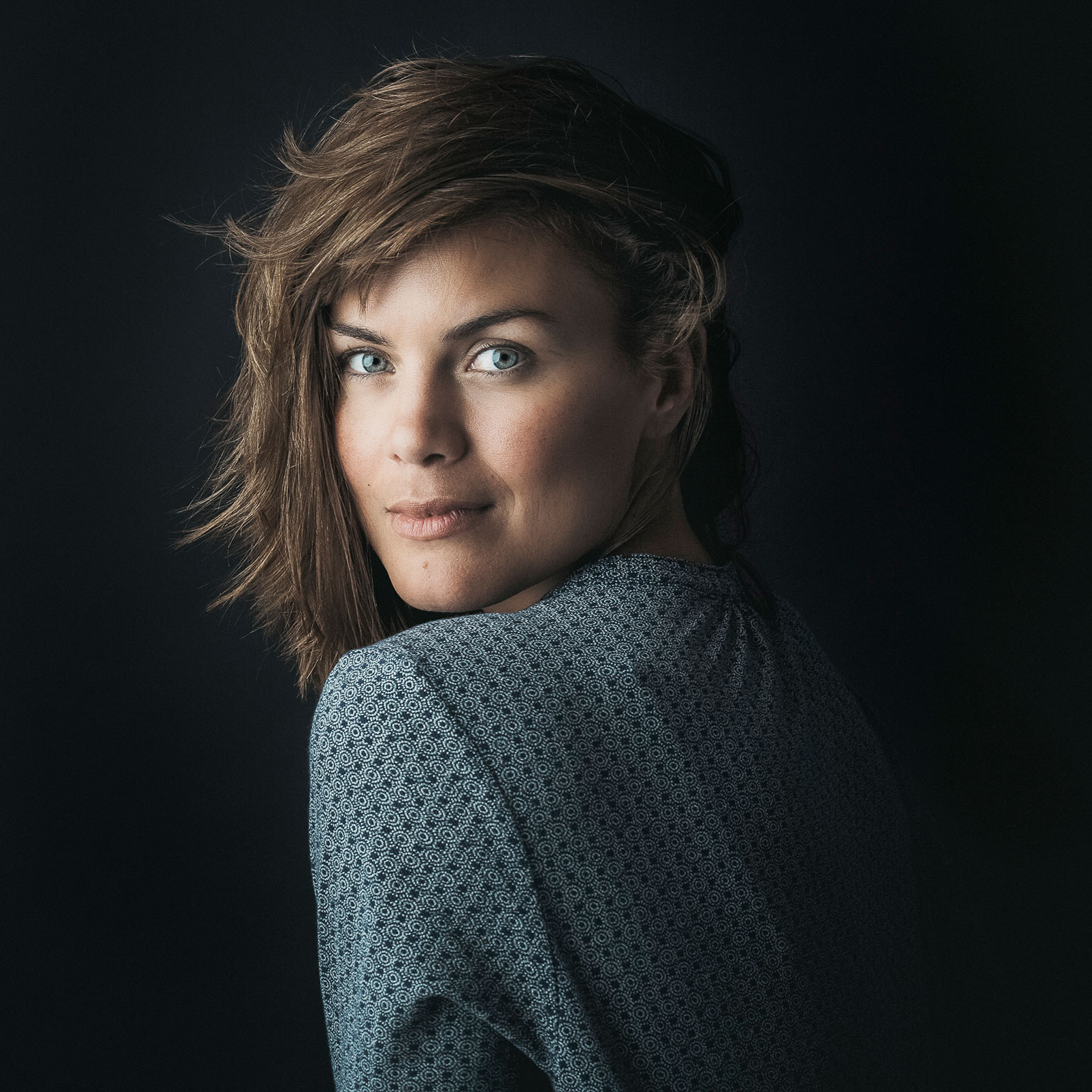 junge Frau in einem einfachen blau-grauen Kleid blickt über die Schulter, offener Blick schöne Augen, Rembrand Stil, Lichtset, one light, Portfolio , EMF Ernst Merkhofer, Portraits,