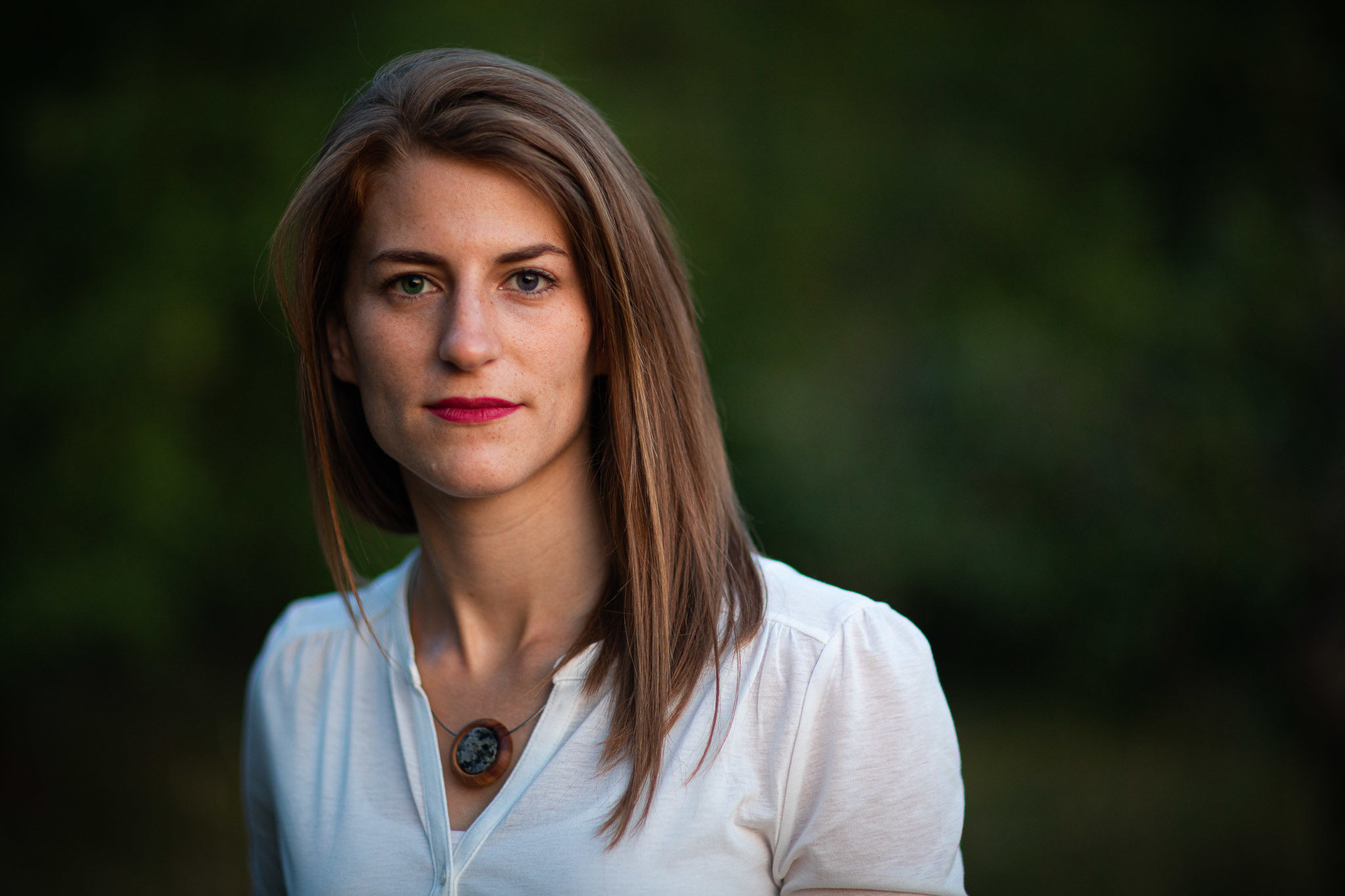 Outdoor portraits einer jungen Frau, blick direkt in die Kamera, Hintergrund dunkels, verschwommenens Blattgrün, offenes sehr weiches Abendlicht nach Sonnenunterang, Outdoor Portraits, Best Light.