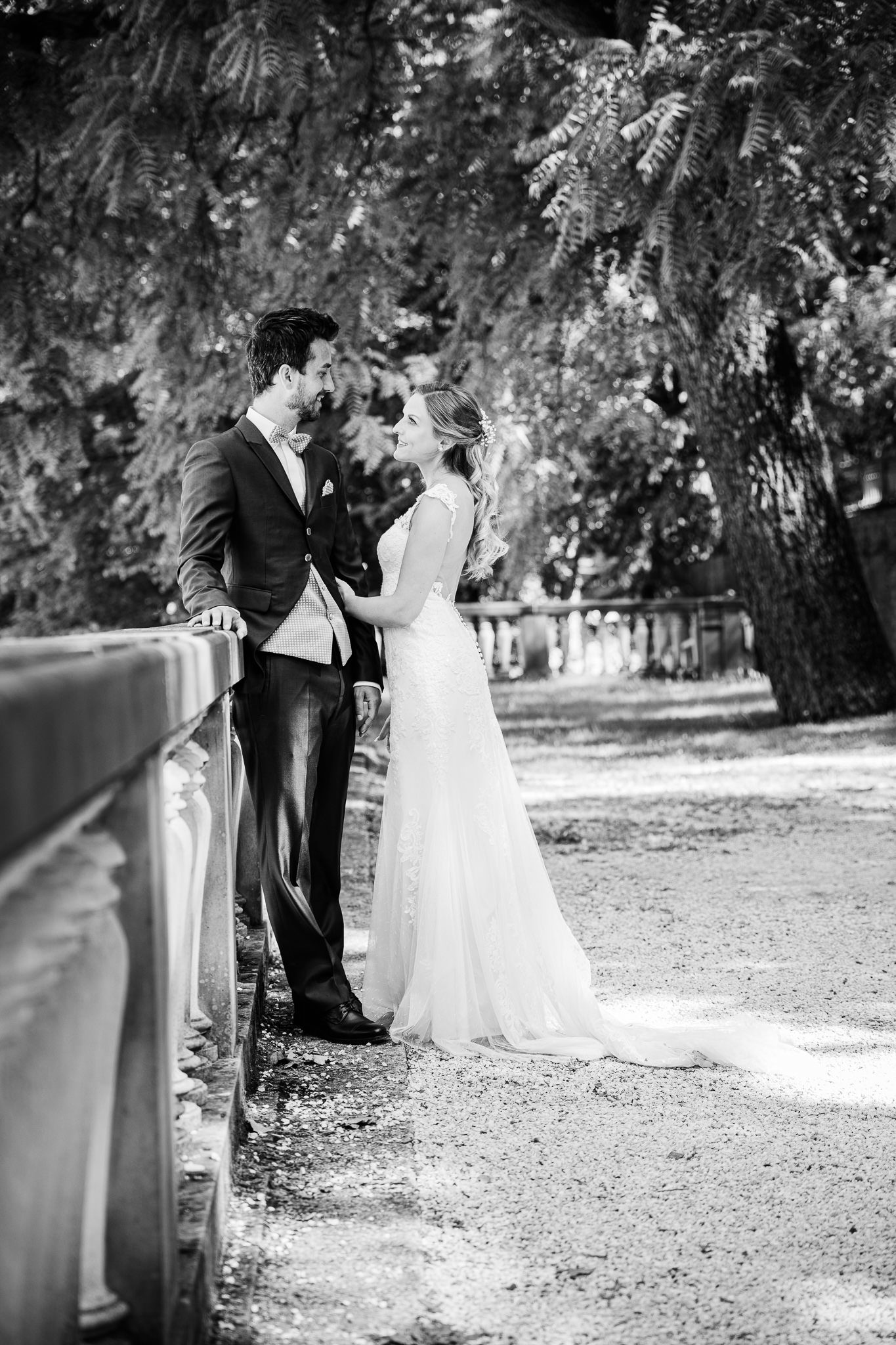junges Brautpaar steht an einem Steingeländer im Heidelberger Schloßpark und schauen sich an. Fotosession nach der Hochzeit.
