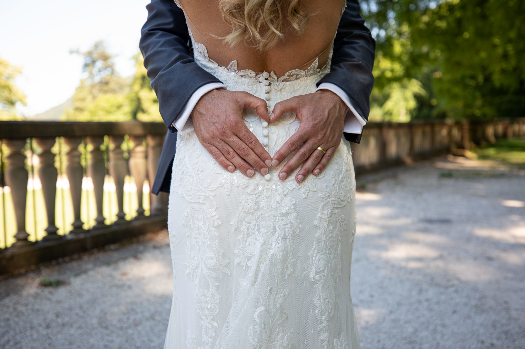 Braut steht direkt vor dem Bräutigam, er formt mit den Händen ein Herz auf Ihrem Rücken. After Wedding Session.