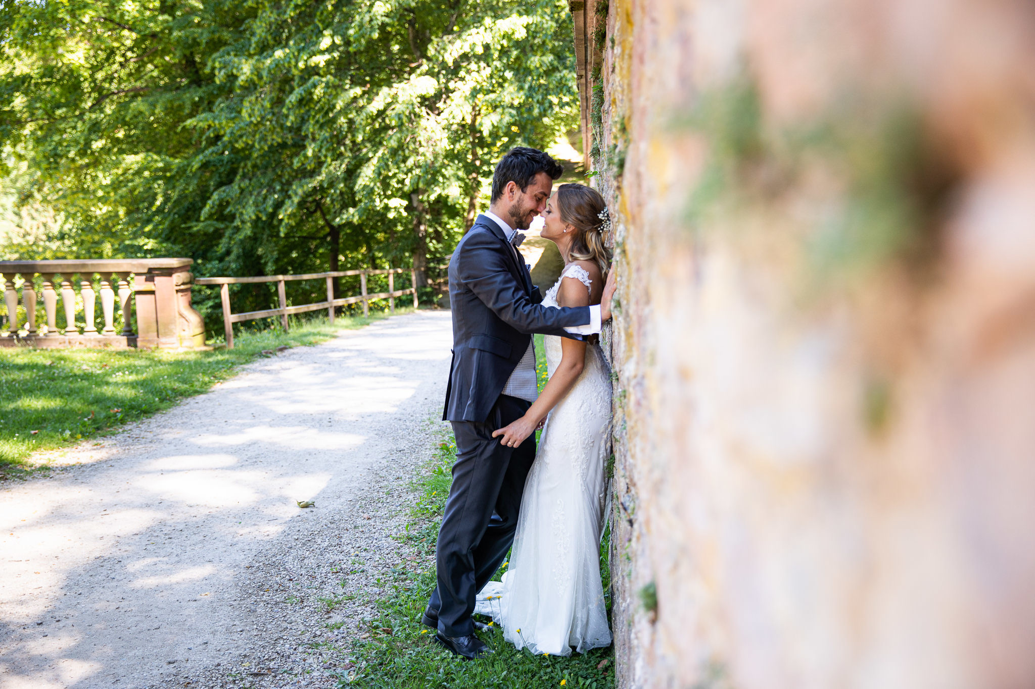 Braut steht mit dem Rücken an einer Steinmauer, der Bräutigam steht direkt vor Ihr und beugt sich Ihr entgegen, inniger Blickkontakt. Bilder nach der Hochzeit, After Wedding Session.