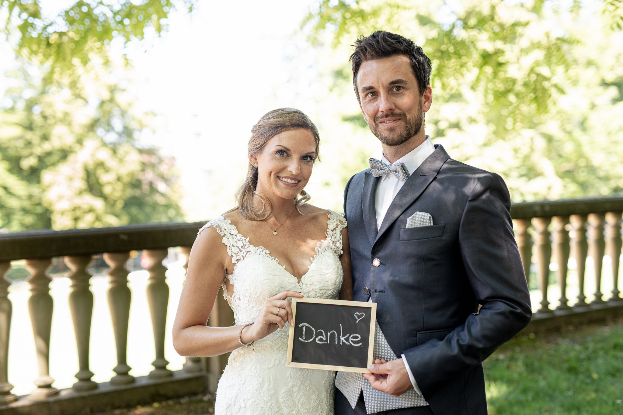 Beispiel für einen Dankeskarte. Braut und Bräutigam halten ein Schiefertäfelchen mit dem Wort Danke vor sich und lächeln in die Kamera. Detail After Wedding Session in Heidelberg.